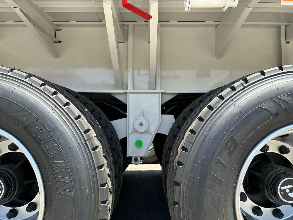 Dual 12R22.5 tires and a mechanical suspension hanger on the four-axle running gear of the long-deck flatbed.