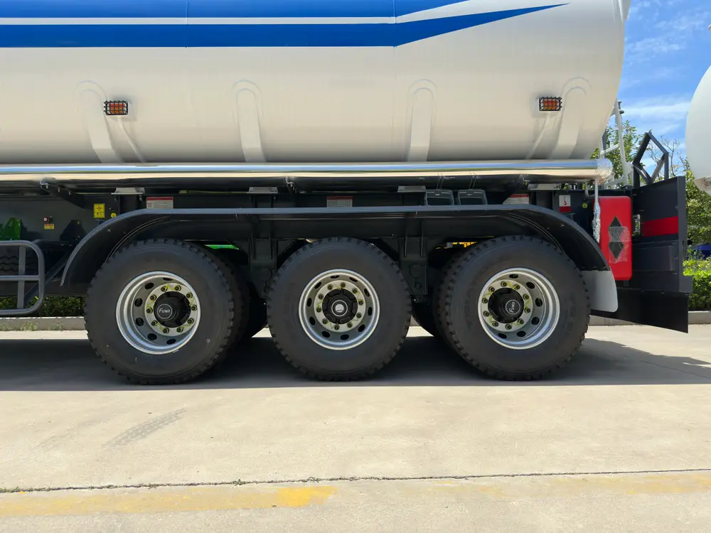 Three-axle running gear of the oil tanker trailer with FUWA hubs, steel rims, and the polished side guard rail.