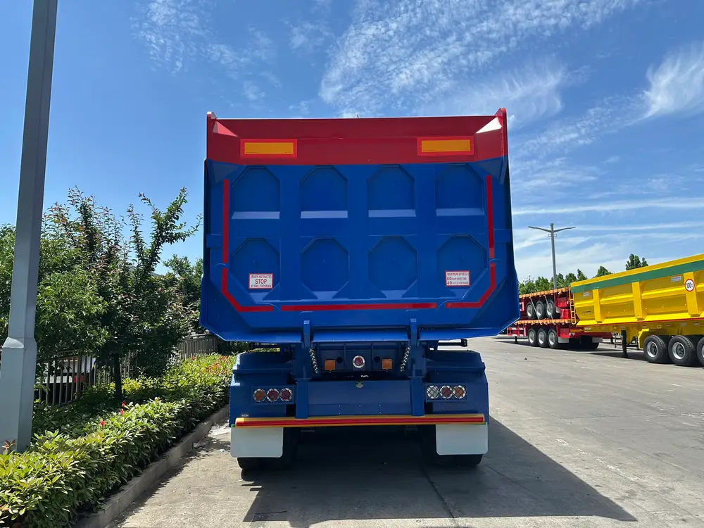 Rear face of the rectangular rock body showing the pressed tailgate panels, red top rail, and export-market safety decals.