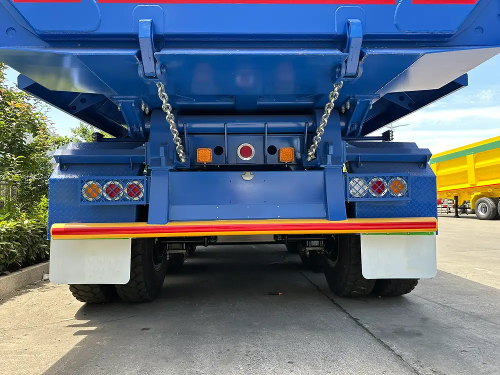 Chain-latched gravity tailgate hardware and caged LED tail lamp clusters on the rear of the 100 ton dump trailer.