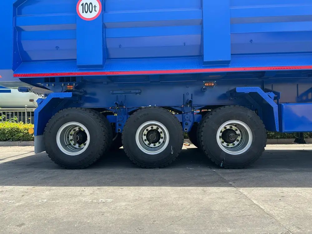 Three-axle running gear with 12.00R20 mining tires and the 100t payload roundel stenciled on the body side.