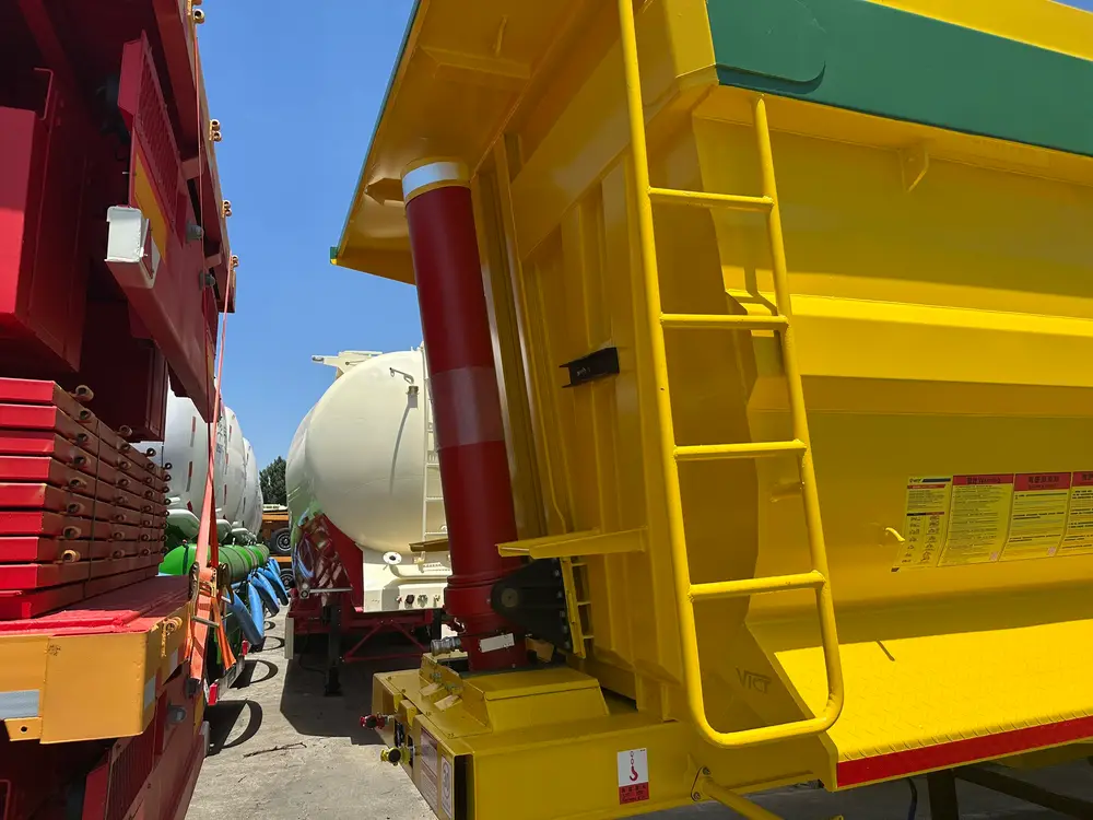 The red HYVA front-mount telescopic cylinder and access ladder on the front wall of the yellow tipper body.