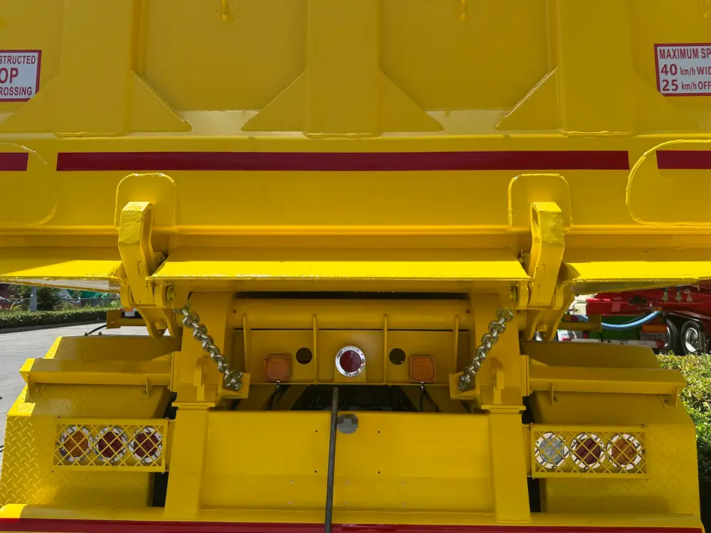 Dual chain-latched tailgate levers and the factory 40 km/h site-speed decal on the yellow tipper body.